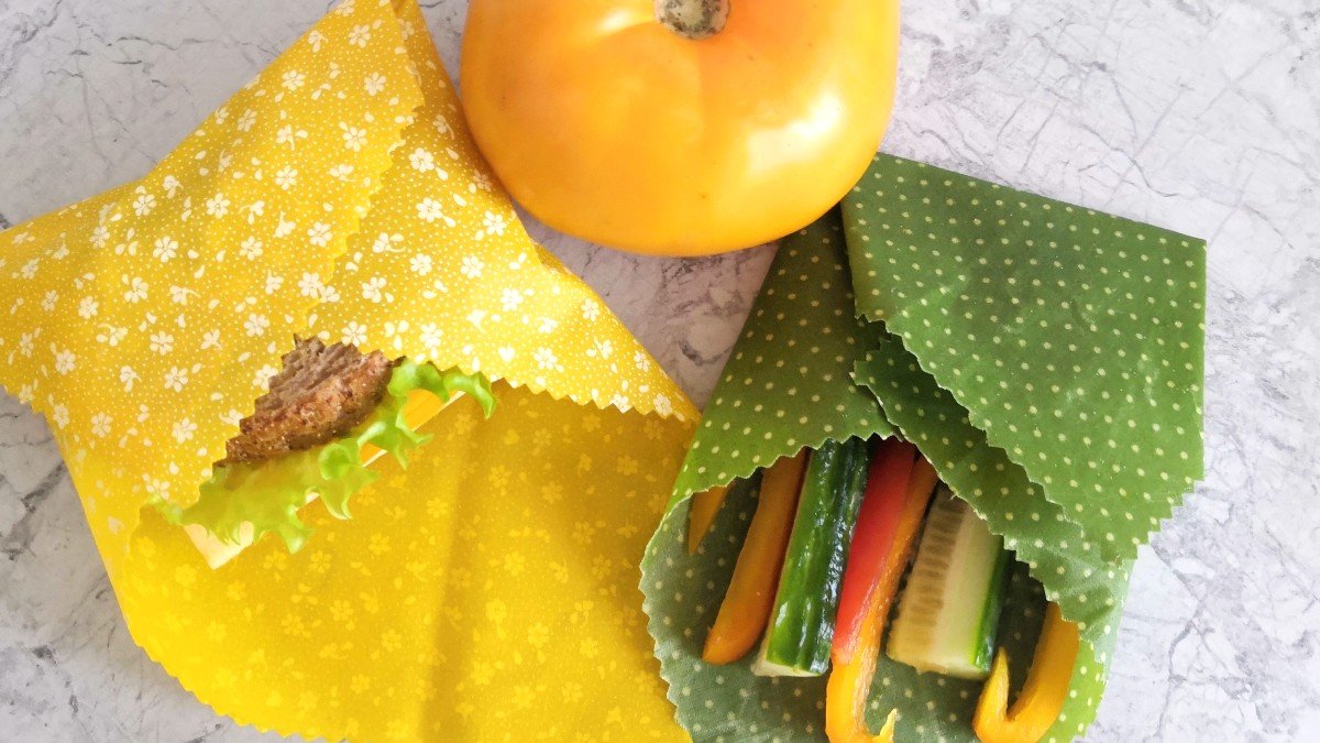 Sandwich, cucumber and bell pepper wrapped in yellow and green beeswax wraps on a counter