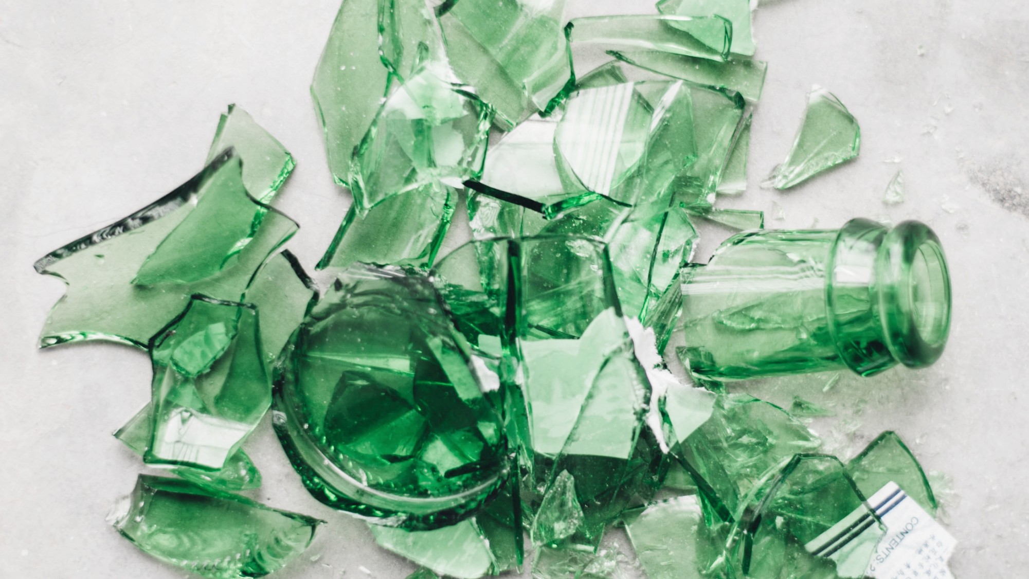 a green glass bottle broken into pieces on a white floor