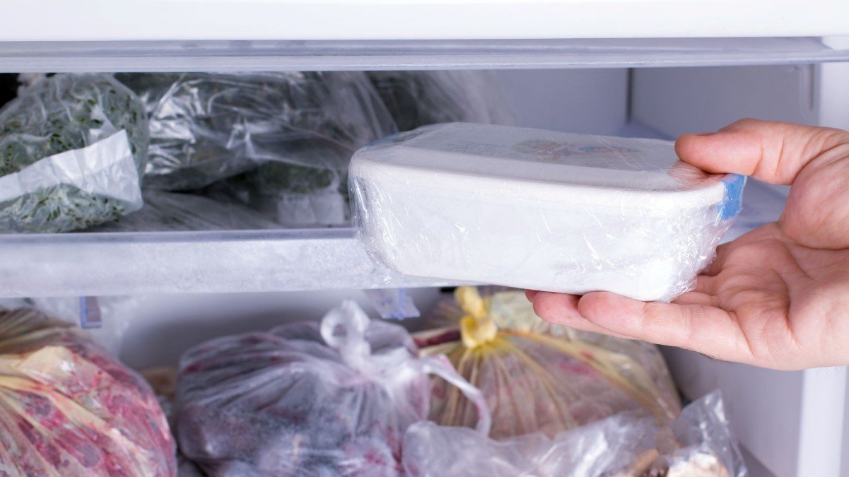 a person taking a white food container out of the freezer