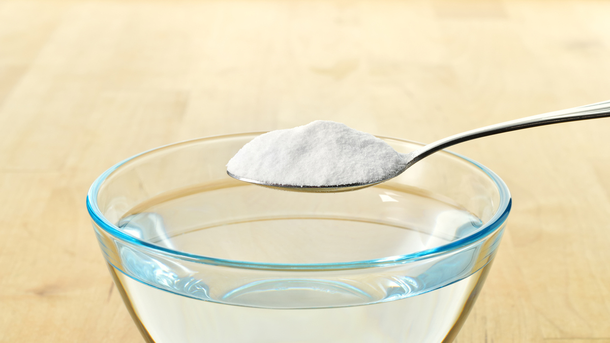 Close-up of baking soda on spoon against background of glass of water.